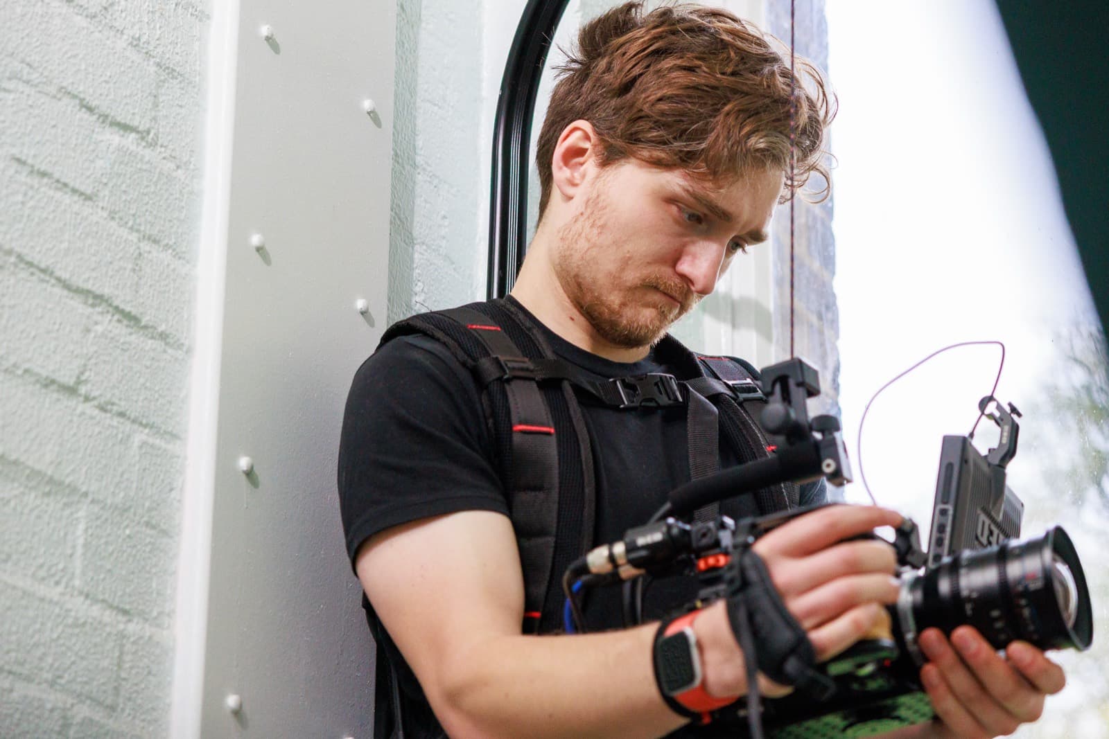 Jack Hobbs in a support vest, working a rigged camera with monitor and radio receiver mounted alongside