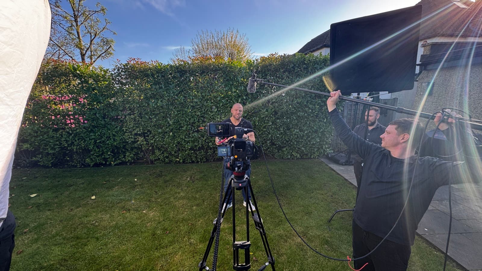 Three of the crew rigging a monitor on a boom arm against a hedge in low autumn sun