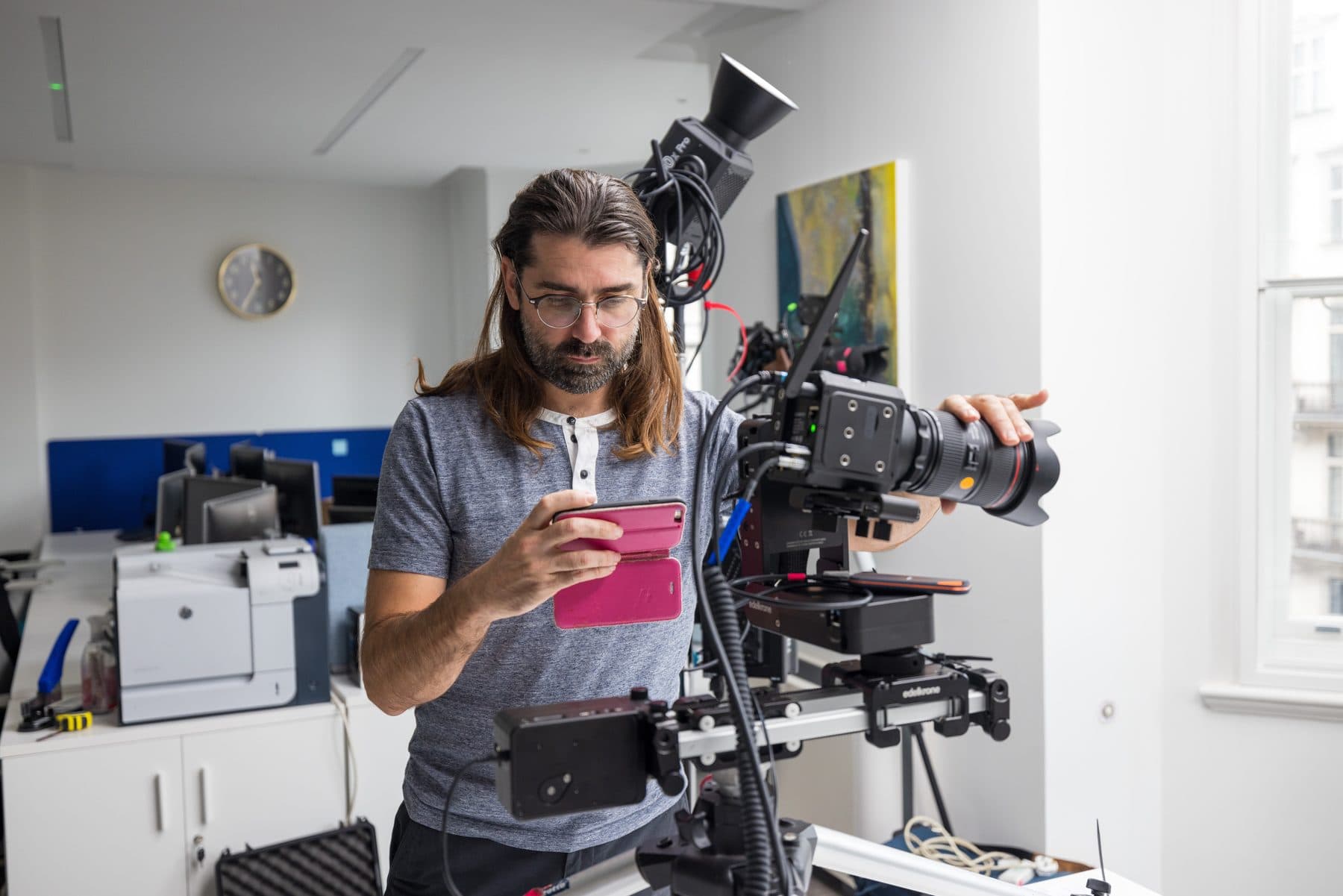 A camera operator building a slider rig in an office, checking the frame on a phone before a take