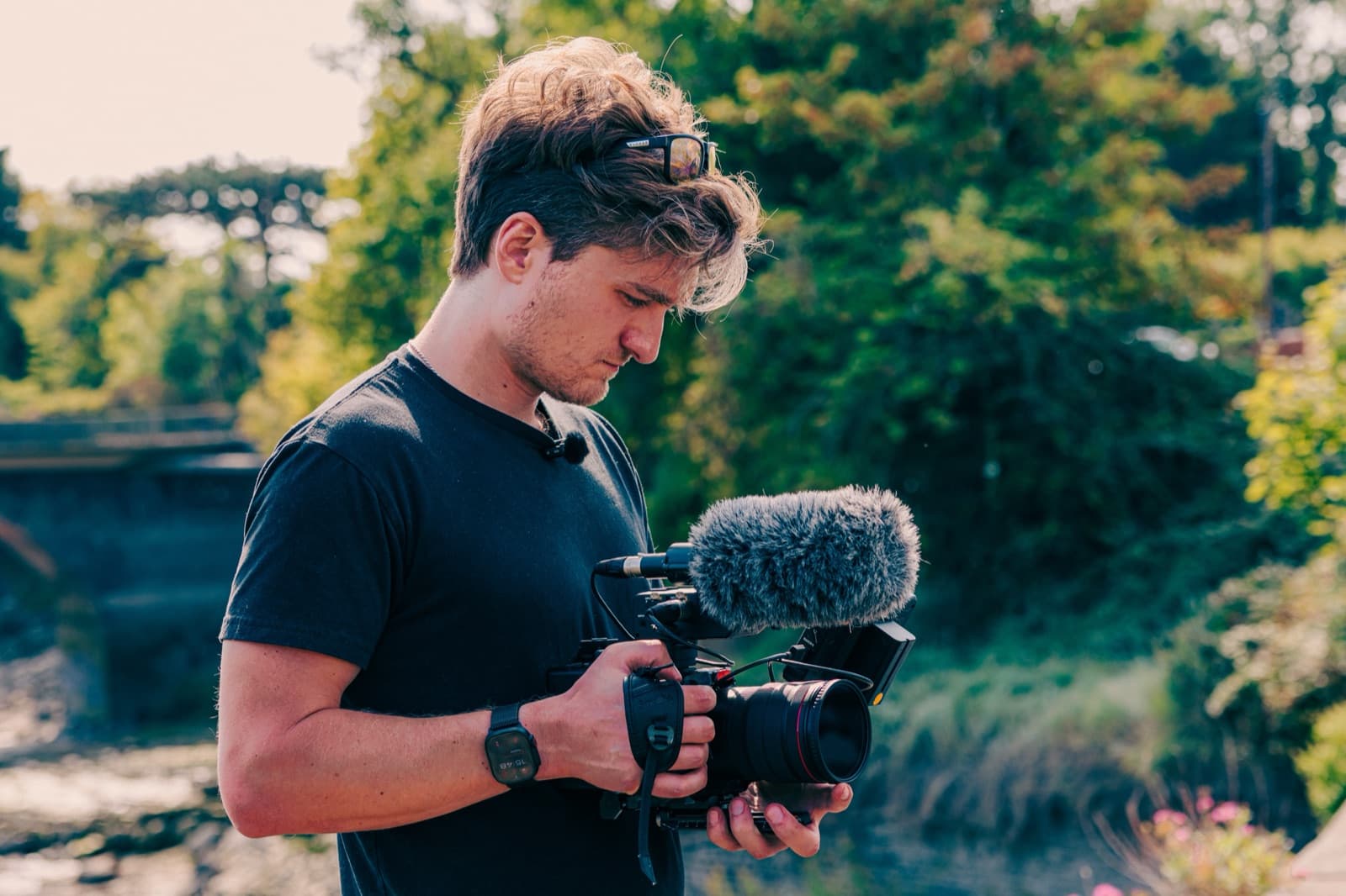A camera operator working handheld on a riverbank, shotgun mic rigged on top