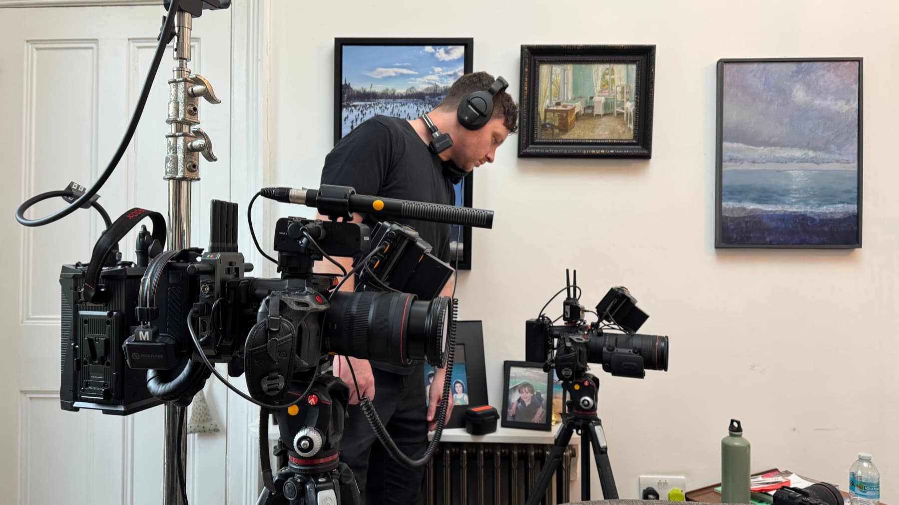 An operator building a camera on location, a second body rigged on sticks beside it and a shotgun mic across the top
