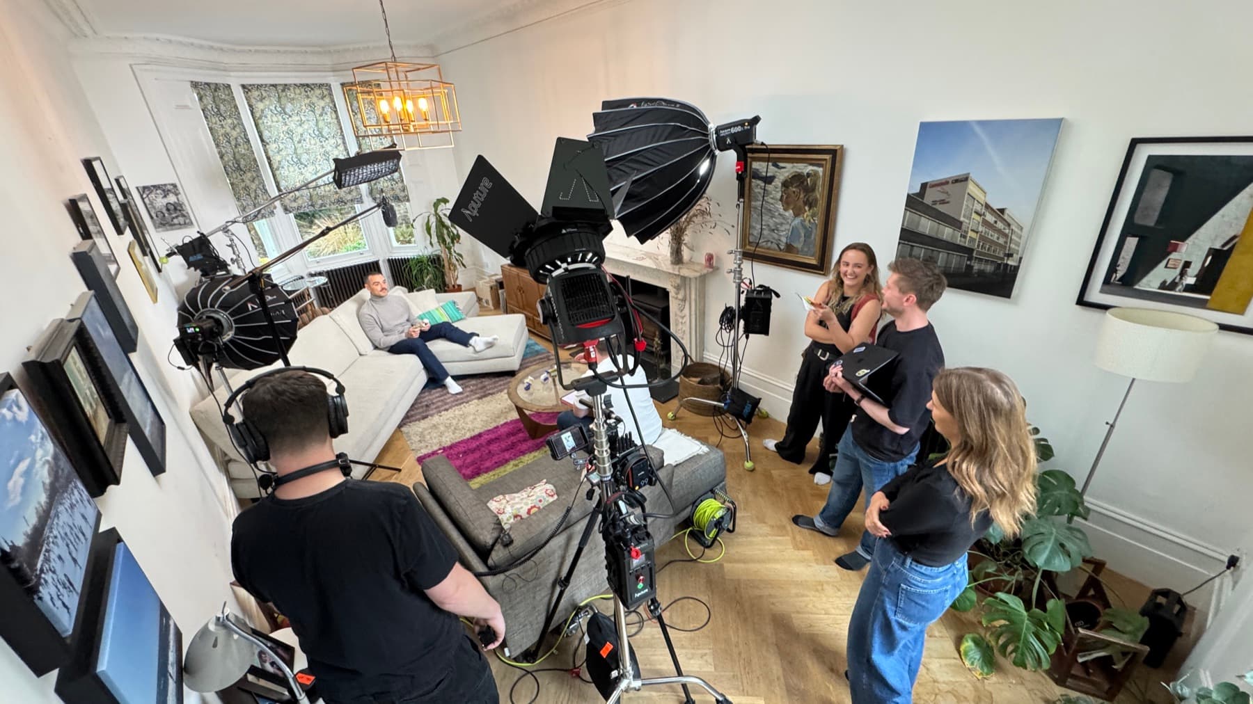 A crew of four working a lit living room, two heads on stands through diffusion and a camera on sticks in the middle of it