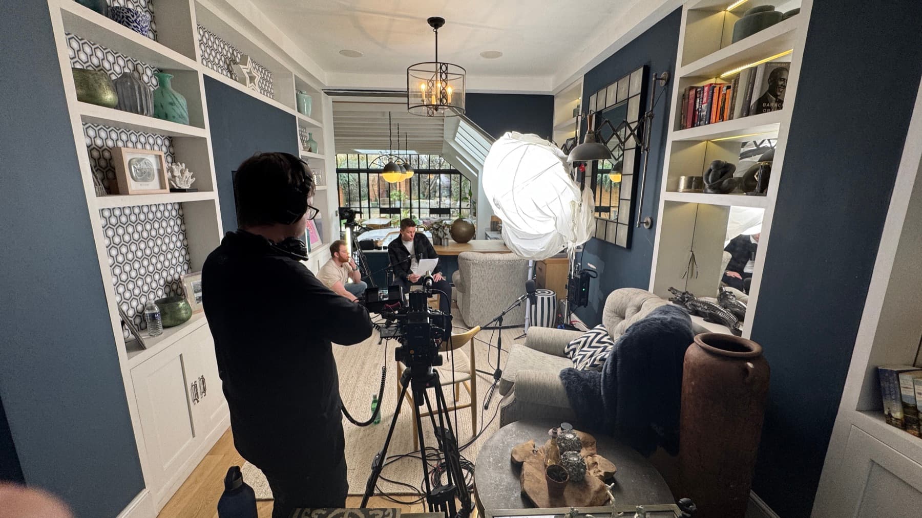 An operator at the camera in a narrow room, a lit practical over the subject at the far end