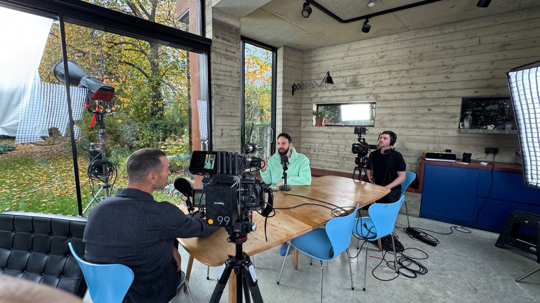 A table interview set up in a concrete and glass room, two cameras and a softbox in, crew either side of the table
