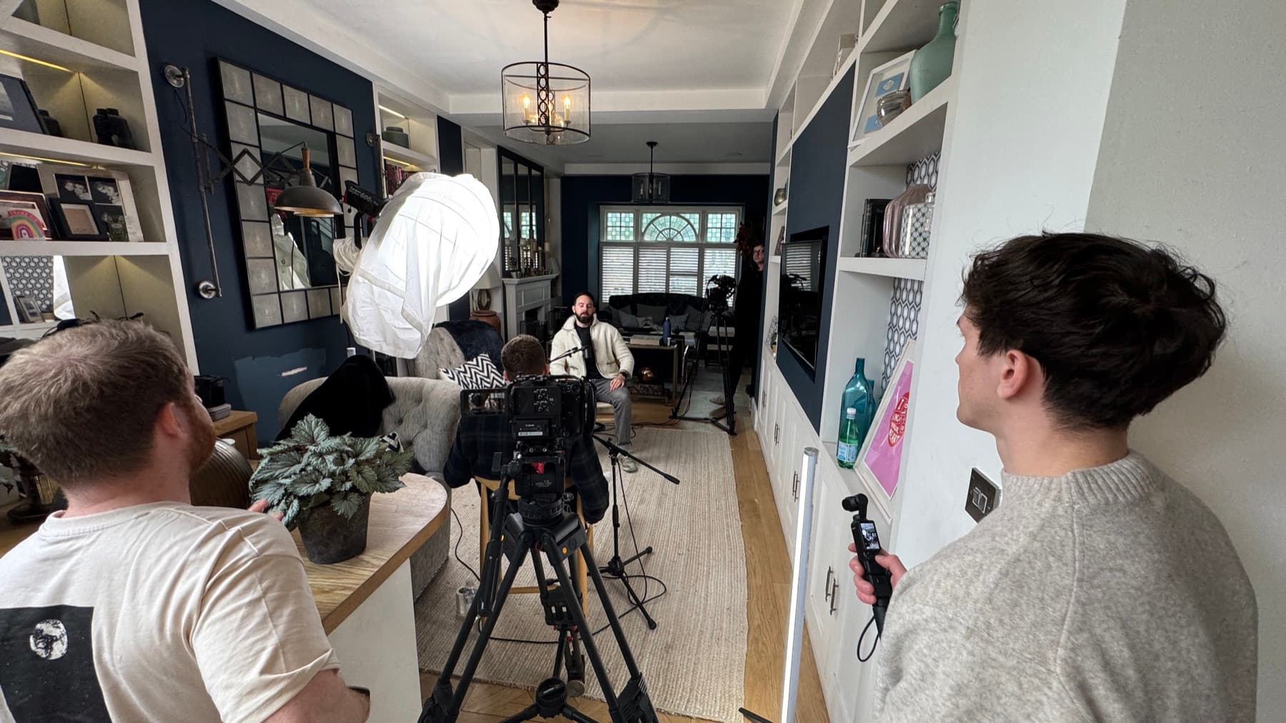 Three of the crew watching a take from behind the camera in a narrow room, gimbal ready in the foreground