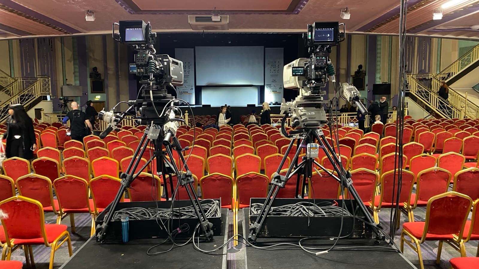 Two cameras locked off on an empty conference room before the audience arrives, cables run and taped down
