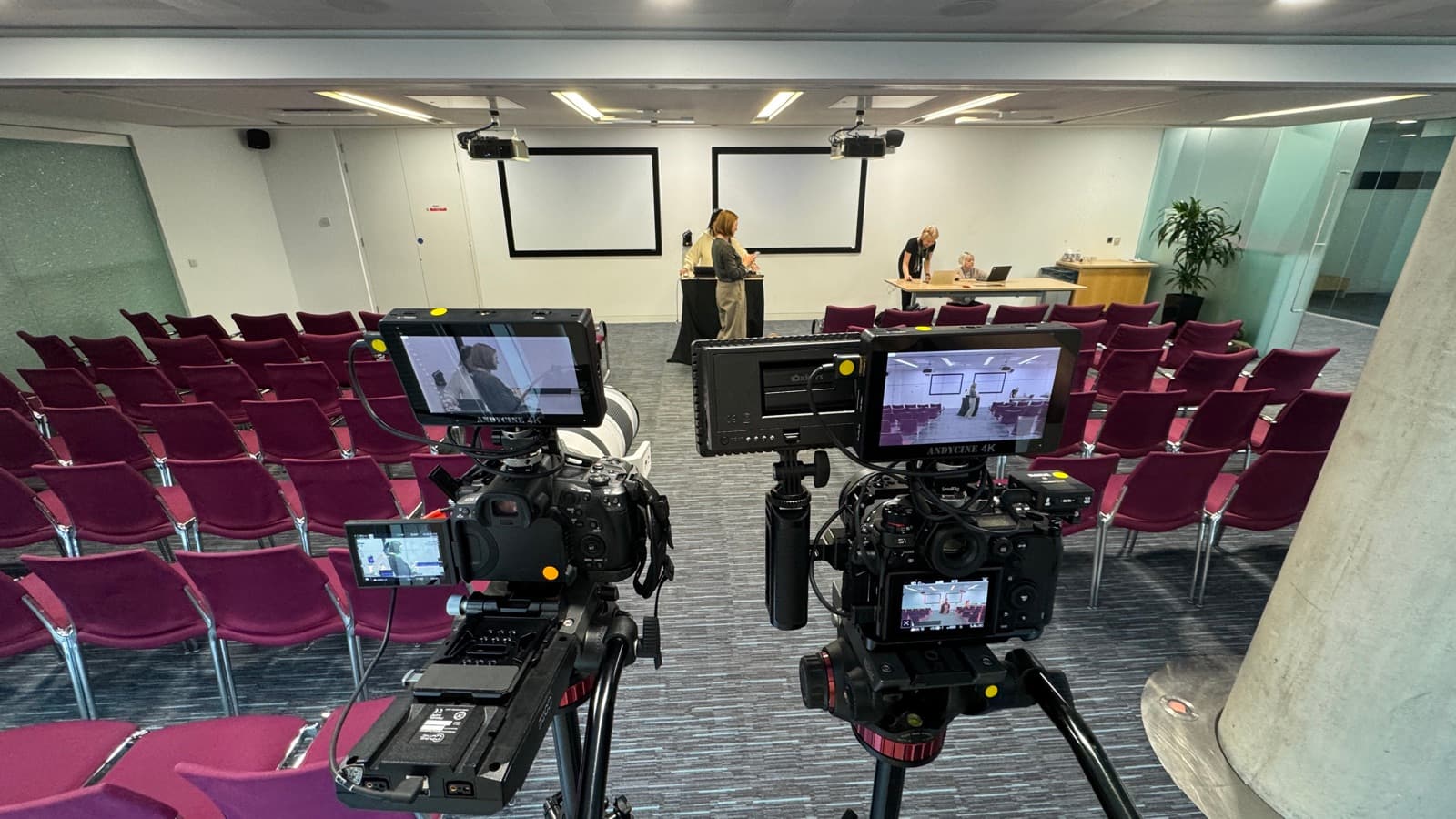 Two cameras covering a speaker at a lectern from the back of a conference room