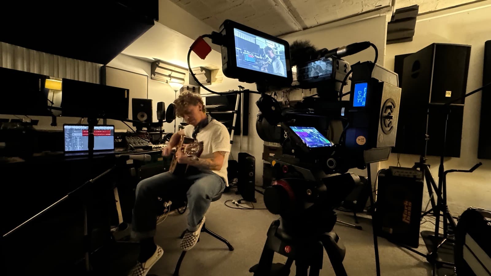 Filming in a recording studio control room, two cameras on the player and the desk monitors still live behind