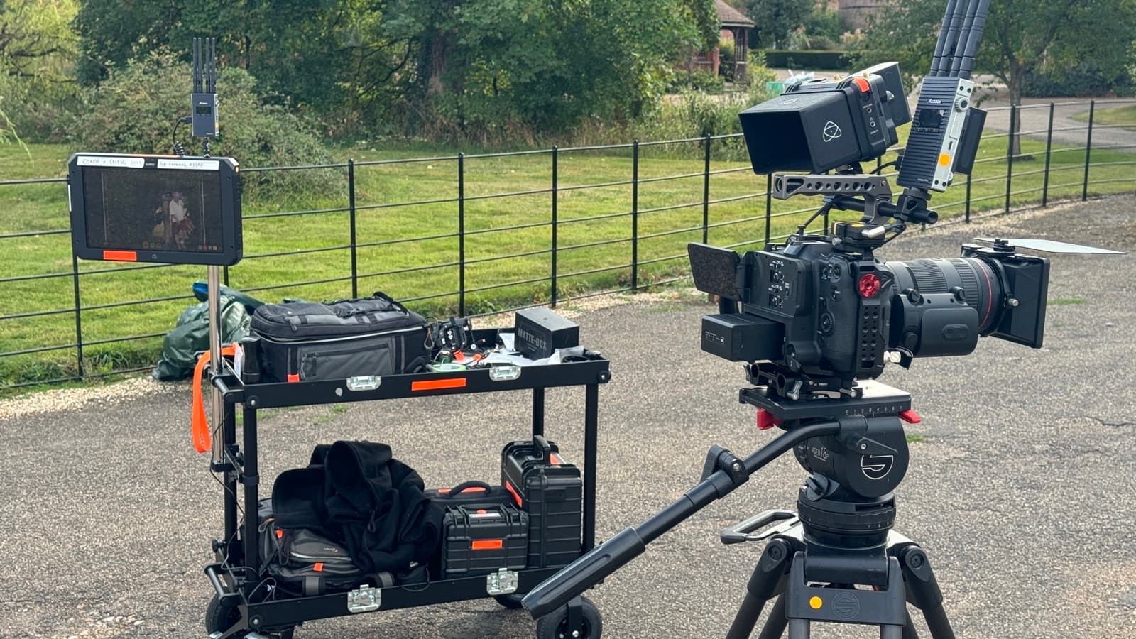 A camera and monitor set up outdoors along a fence line, second body and case ready on the ground