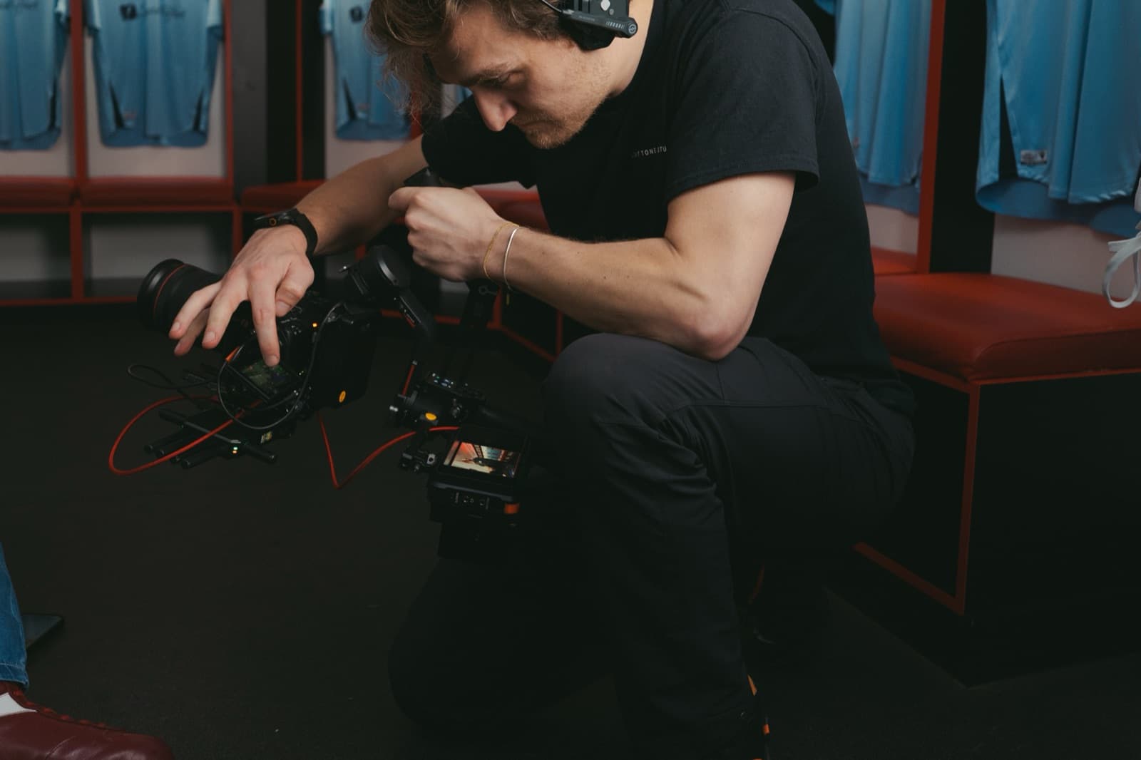 An operator crouched over a camera build in a dressing room, headphones round the neck