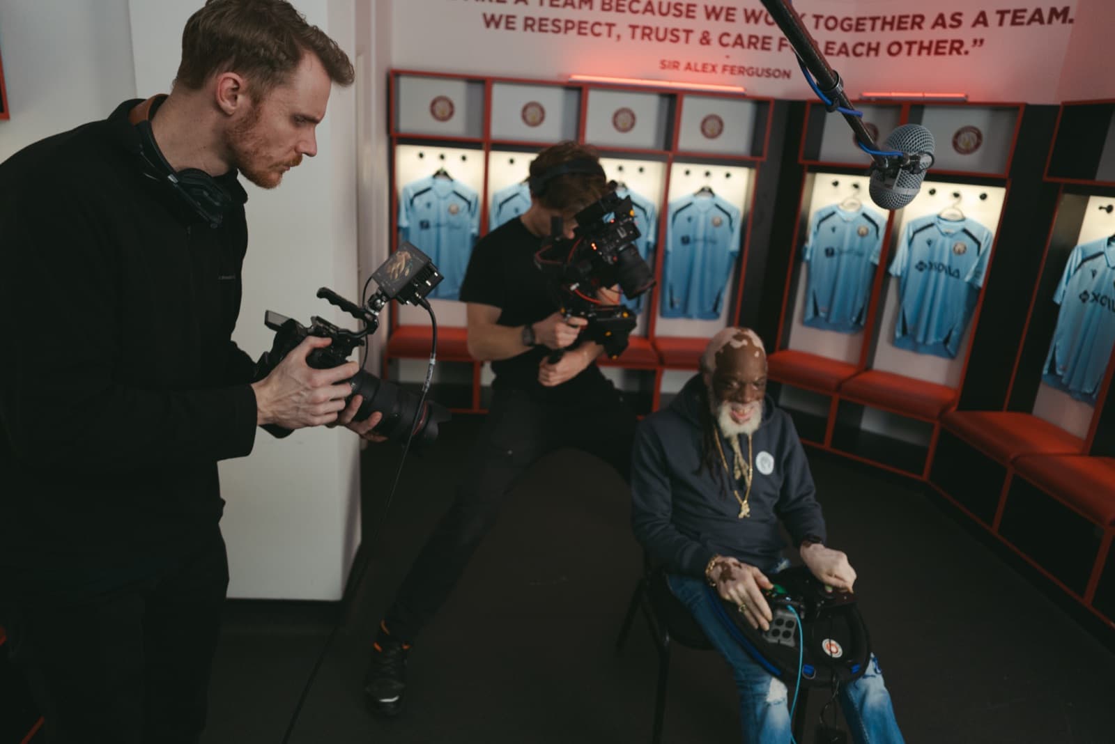 Two cameras covering a contributor seated in a football dressing room