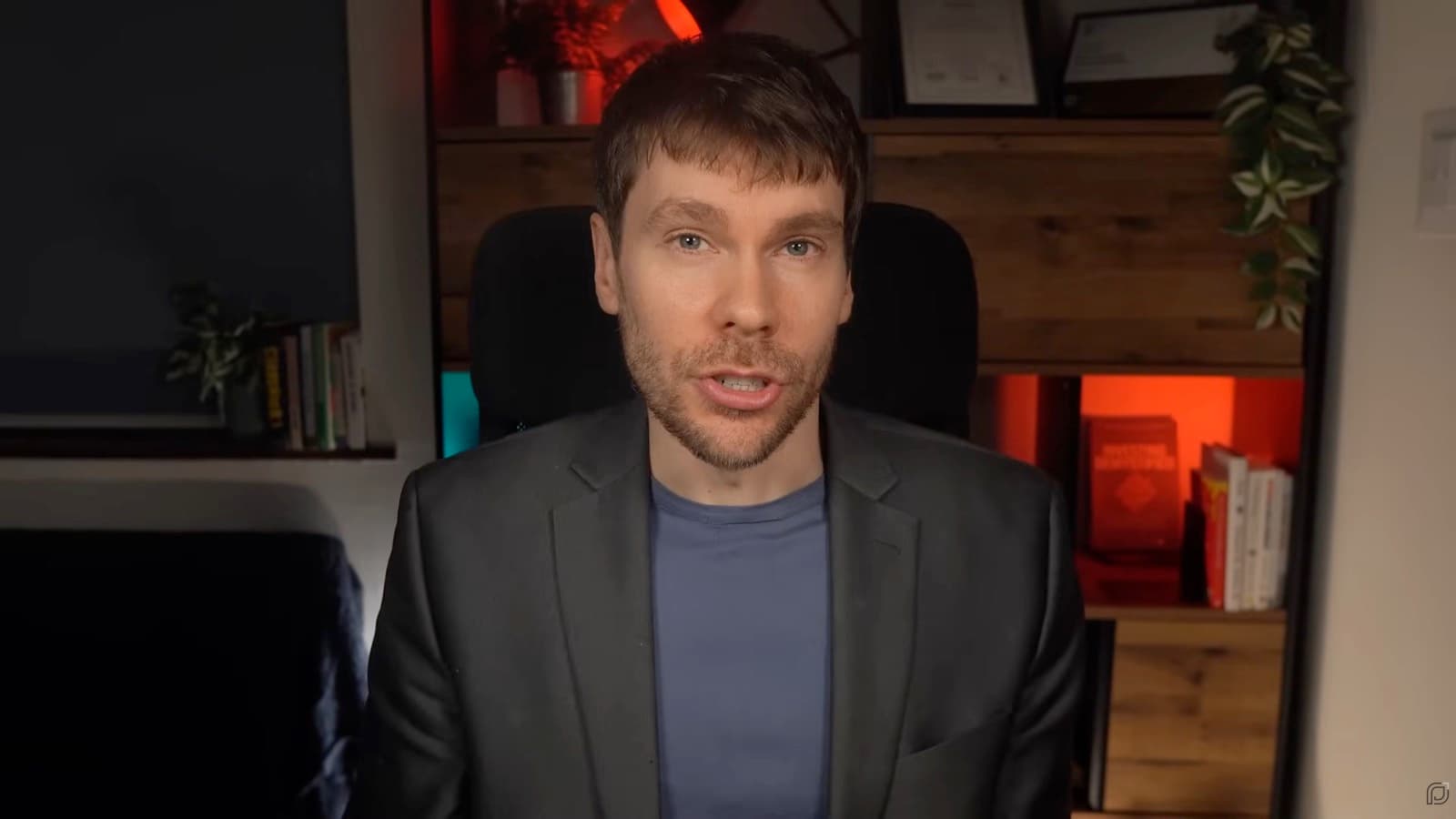 The same desk after: an even key on his face, the microphone out of shot, the shelves behind him lit deliberately
