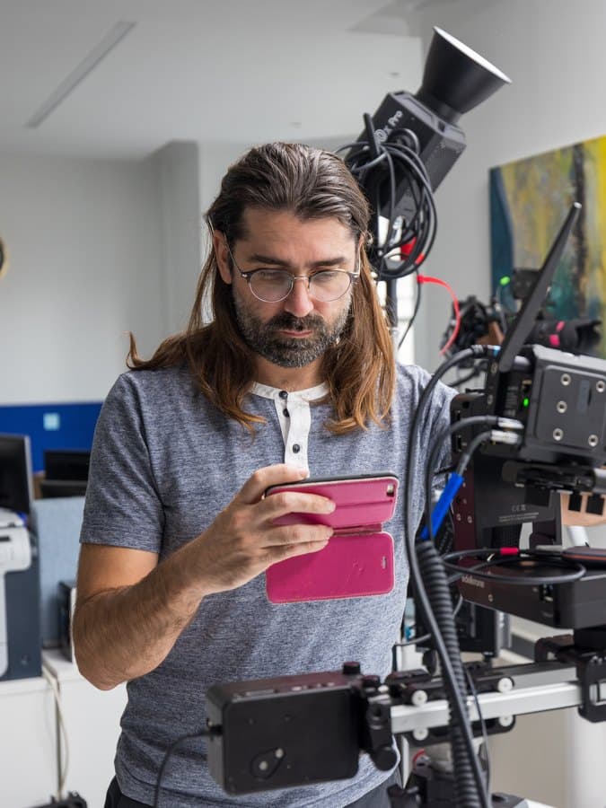 Alex Martin-Verdinos setting up a slider rig in an office, checking the frame on a phone