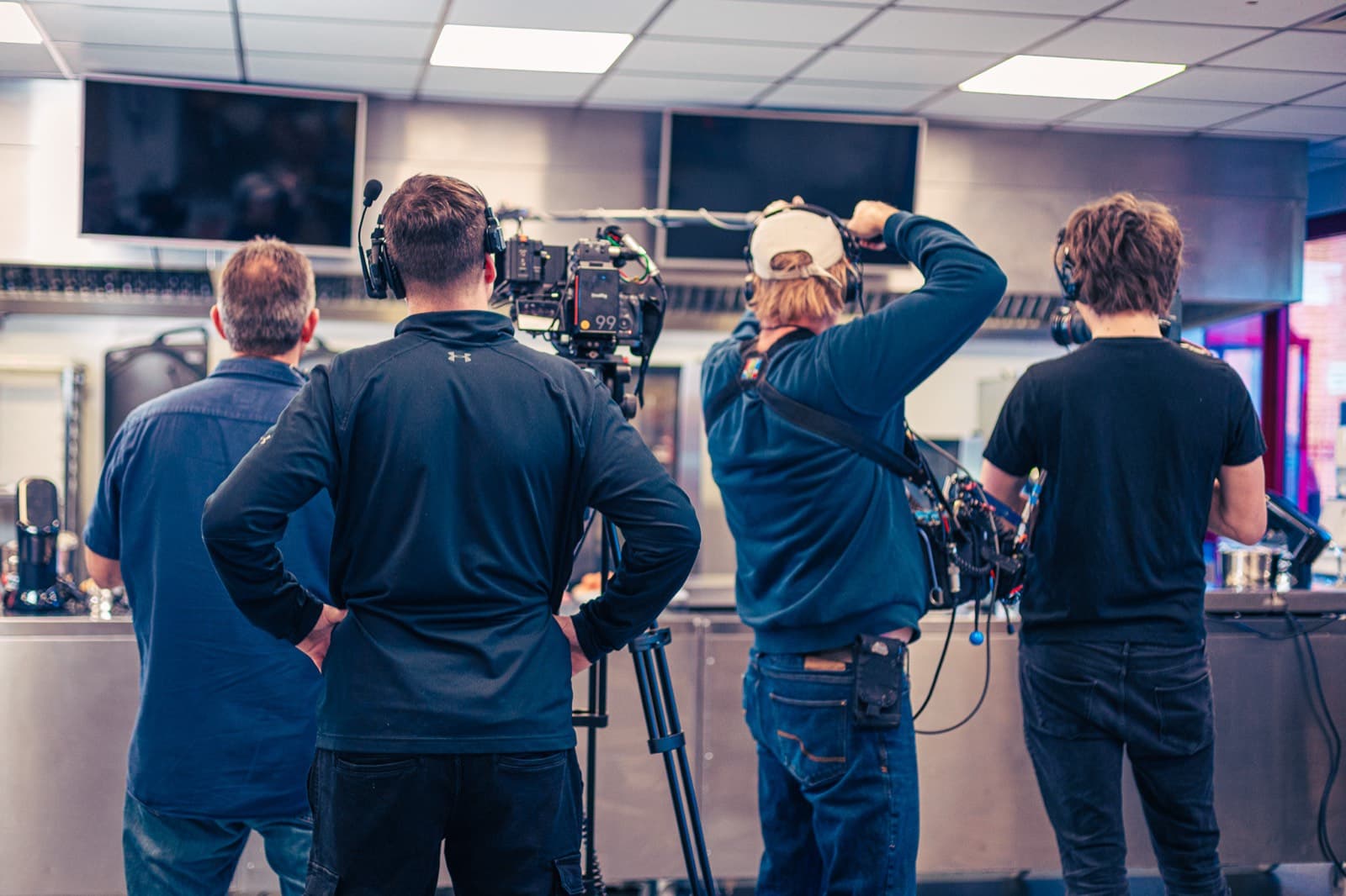 Four of the crew watching a take from behind the camera in a competition kitchen