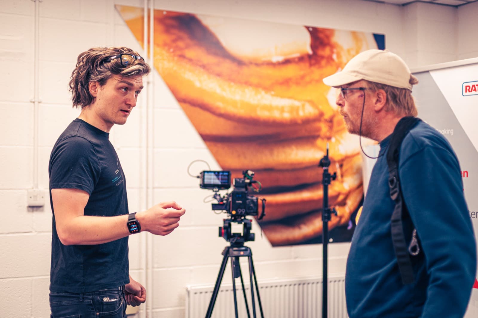 Two of the crew talking a shot through either side of the camera, a food print on the wall behind